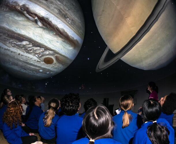 School children look up at two planets projected onto a planetarium
