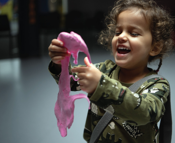 A little girl laughs while stretching pink slime