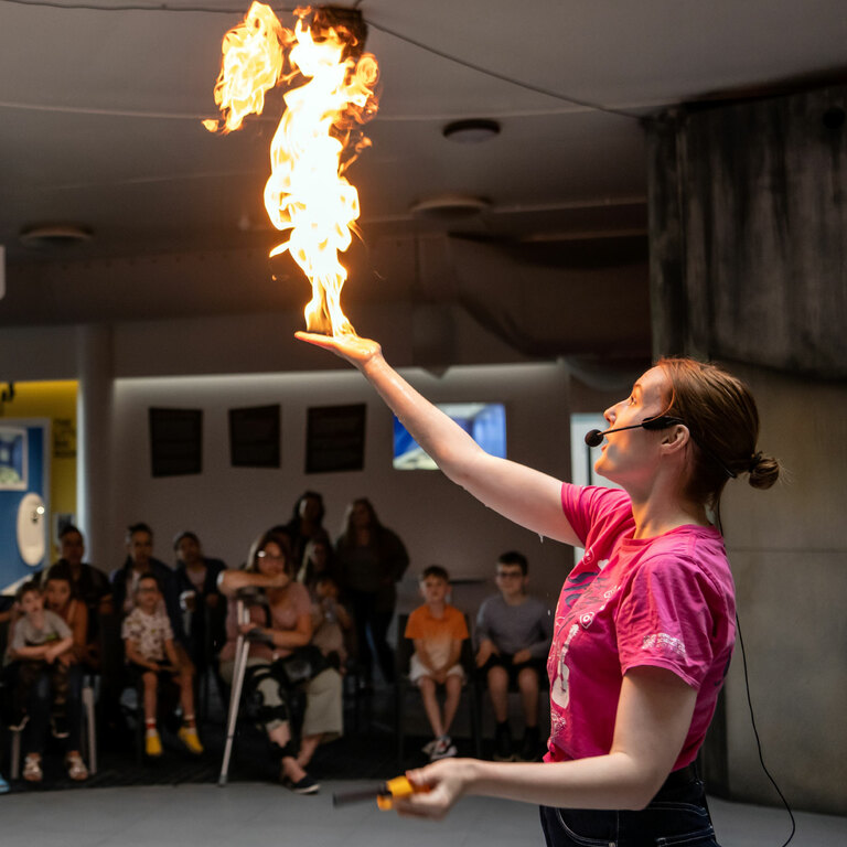 A science communicator in a pink t-shirt is holding fire