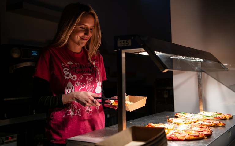 A girl serving pizza at an evening event