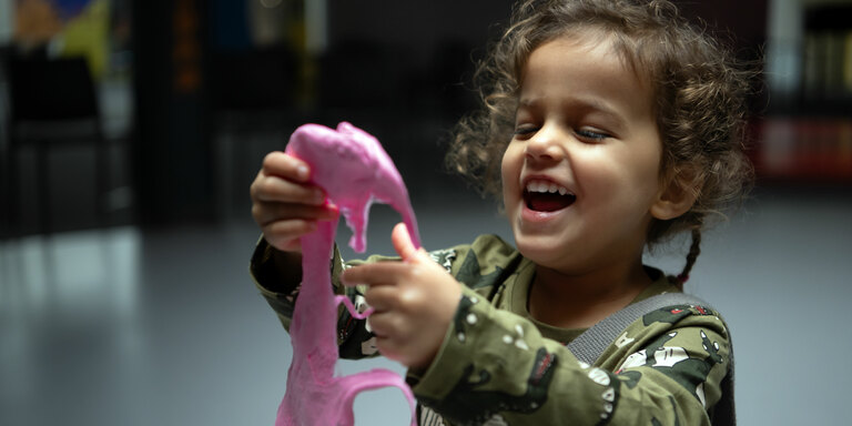 A little girl laughs while stretching pink slime