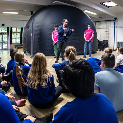 Children watch a science communicator who is stood in front of a mobile planetarium