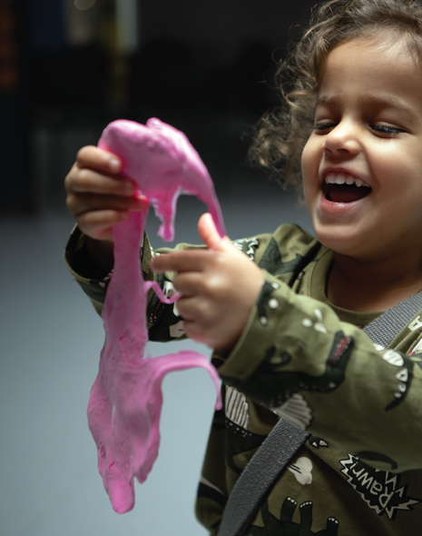 A little girl laughs while stretching pink slime