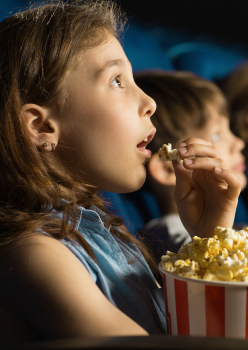 A little girl eats popcorn while watching a film