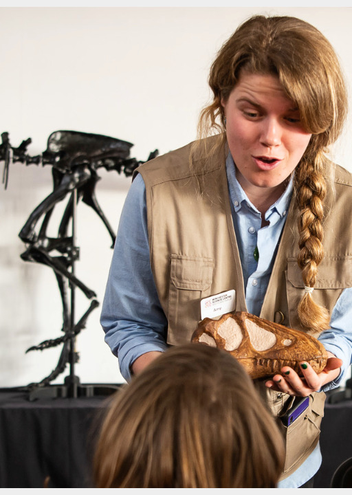 A female presenter showing children a fossil