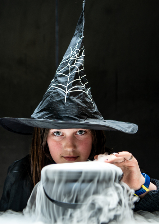 A child dressed as a witch places their hand over a cauldron filled with dry ice vapour