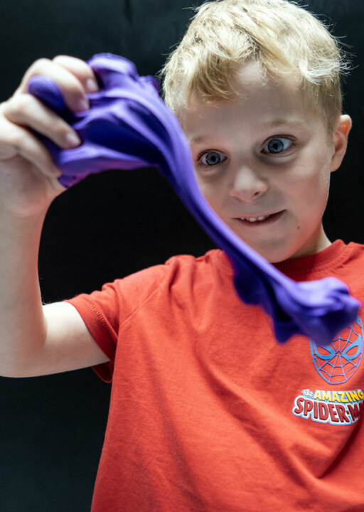 A little boy stares in wonder as he stretches some purple slime